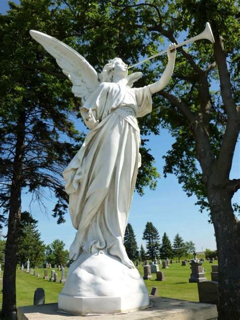 a statue of an angel playing the trumpet in a cemetery with trees and blue sky behind it