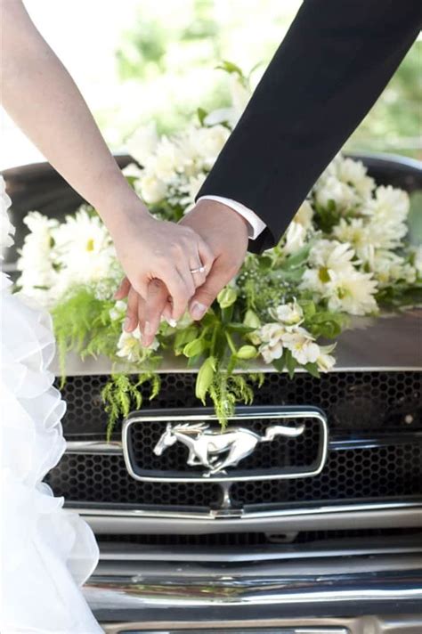 the bride and groom are holding hands in front of a car with flowers on it