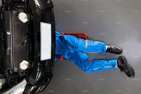 Mechanic in blue uniform lying down and working under car at the garage ...