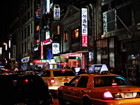 a busy city street at night with neon signs and cars parked on the side of the road