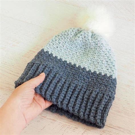 a hand is pointing at a knitted hat with a pom - pom