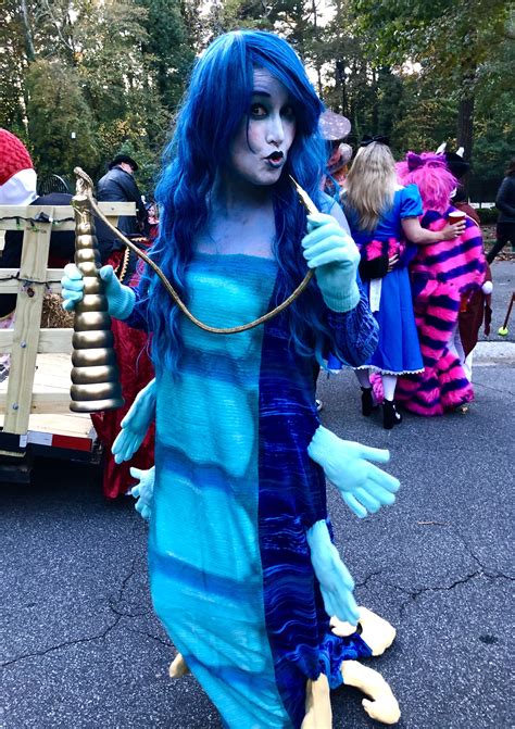 a woman dressed as a mermaid with blue hair and makeup, holding a stick in her hand