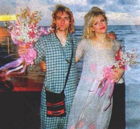 two people standing next to each other in front of the ocean with flowers on their arms