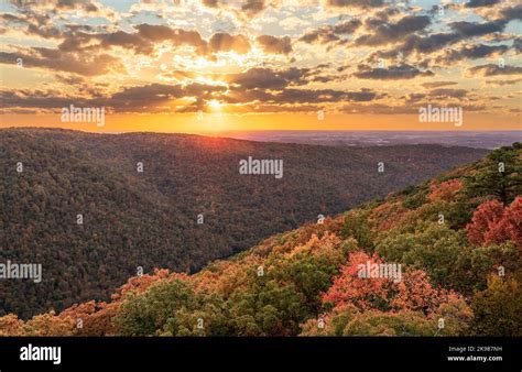 Sun setting behind clouds illuminating the fall colors of the trees in ...