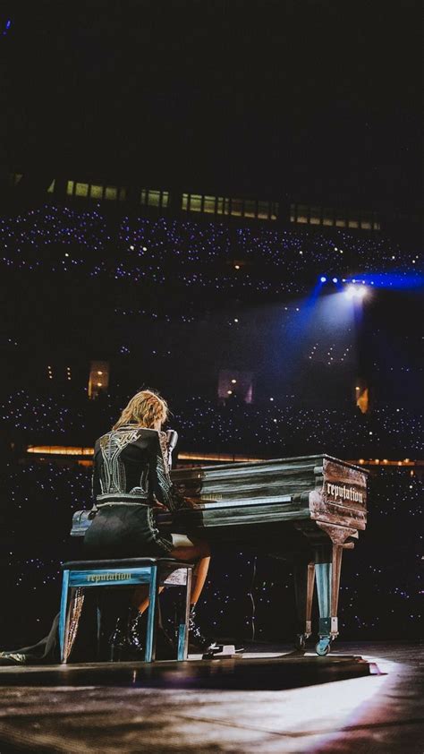 a woman sitting at a piano in front of a stage with spotlights on it