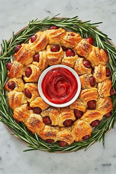 a platter filled with pigs in a blanket and topped with ketchup on rosemary sprigs