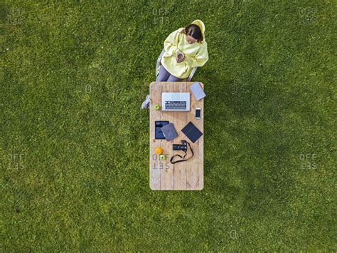 Aerial view of woman sitting at coffee table set on green lawn with mug of coffee in hands stock ...