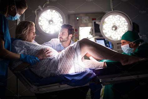 Doctor examining pregnant woman during delivery while man holding her hand in operating room ...