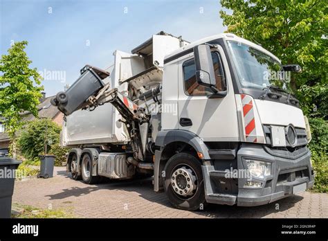 automated garbage collection - hydraulic side loader of a white garbage truck grabs the garbage ...