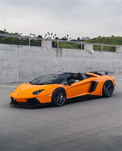 an orange sports car parked in a parking lot next to a concrete wall and fence