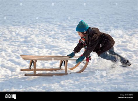 Little boy pushing sled uphills in the snow Stock Photo - Alamy