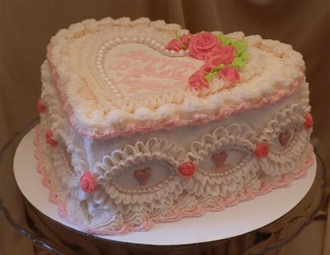 Heart shaped sour cream white cake covered in cherry flavored butter cream. Embellished with fon ...