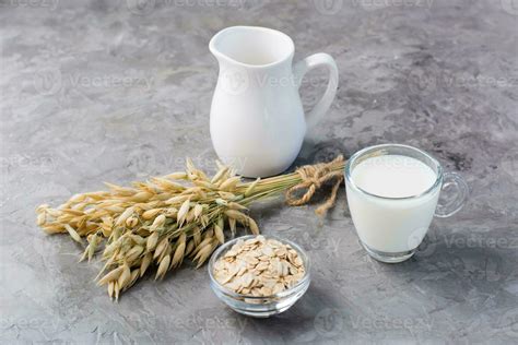 Oat milk in a cup, oatmeal and ears of corn on the table. Alternative to cow's milk. Healthy ...