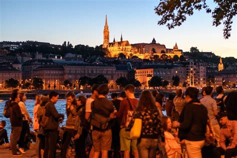 a group of people standing next to each other near the water at night with buildings in the ...