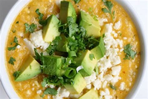 a white bowl filled with yellow soup topped with avocado and feta cheese