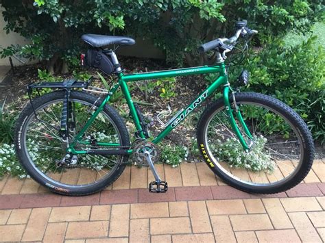 a green bike parked on the side of a brick road next to bushes and trees