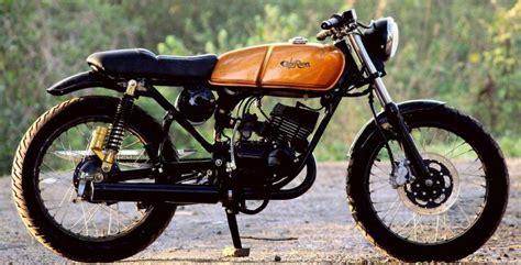 a black and brown motorcycle parked on top of a dirt road in front of trees