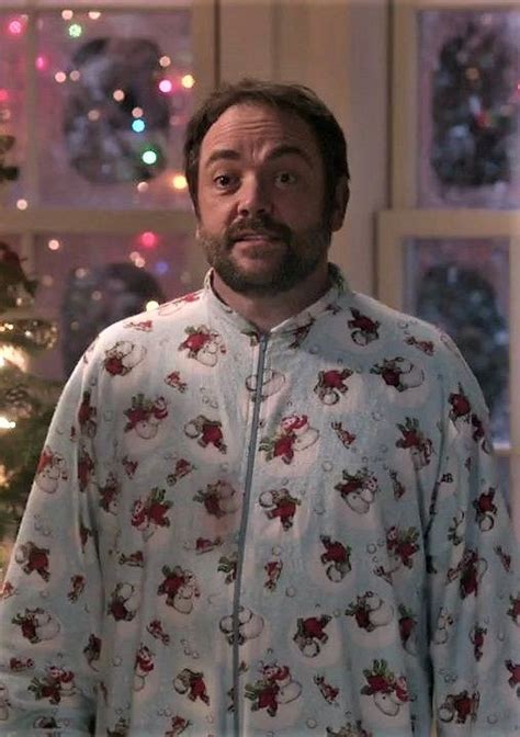 a man in pajamas standing next to a christmas tree