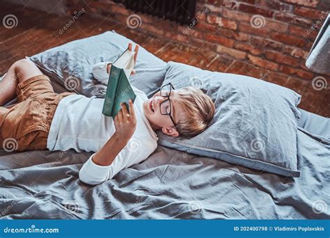 Cheerful Preschool Boy Reading a Book and Lying Down on a Bed Stock Photo - Image of glasses ...