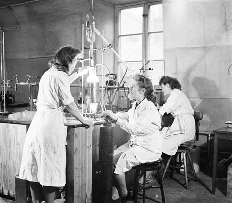 three women in white lab coats are working on an experiment while another woman looks on