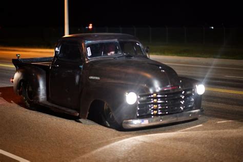 an old truck is parked on the side of the road at night with its lights on