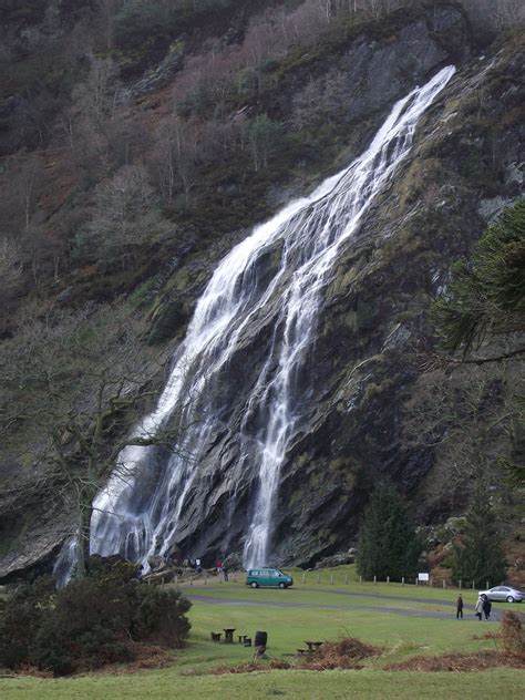 people standing in front of a waterfall with cars parked below it and ...