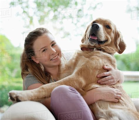 Smiling girl hugging dog on sofa - Stock Photo - Dissolve