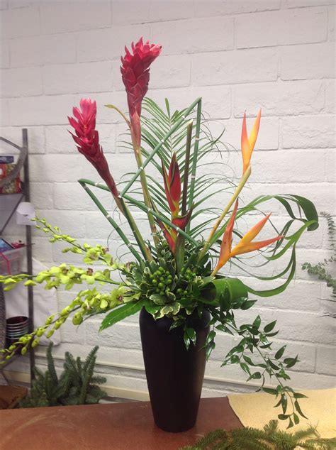 an arrangement of tropical plants in a black vase on a wooden table ...