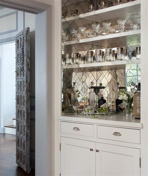 Stunning bar boasts white bar shelves mounted on antiqued mirrored herringbone backsplash tiles ...