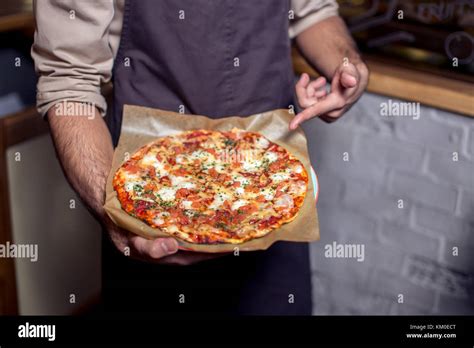 Happy pizza delivery man showing fresh pizza in a commercial kitchen Stock Photo - Alamy