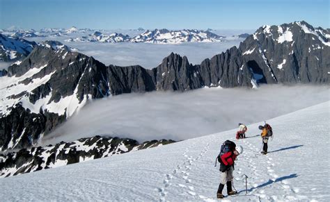 three people hiking up the side of a snow covered mountain with mountains in the background