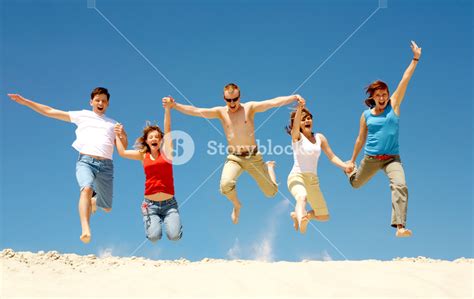 Photo of excited people jumping on sandy beach with their arms raised ...