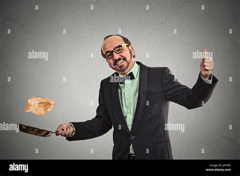 Happy smiling man tossing pancakes on frying pan isolated on grey wall ...