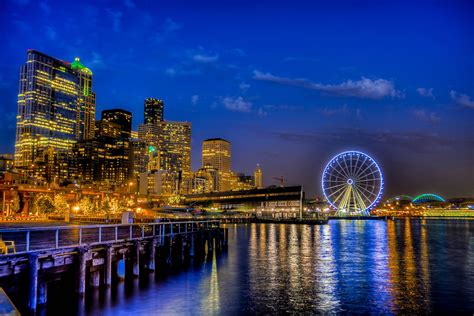 the city skyline is lit up at night with ferris wheel in foreground and ...