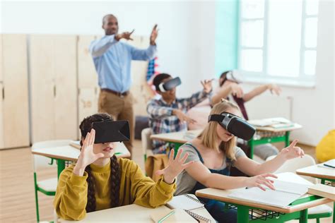 High school teenage students using virtual reality headsets and gesturing teacher standing ...