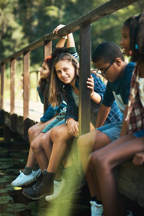 Shot of a group of teenagers sitting on a bridge in nature at summer camp | Interface Children ...