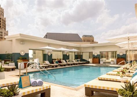 an outdoor swimming pool with lounge chairs, umbrellas and tables in the foreground