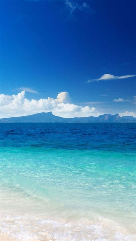 the beach is clear and blue with waves coming in to shore, while an island sits in the distance