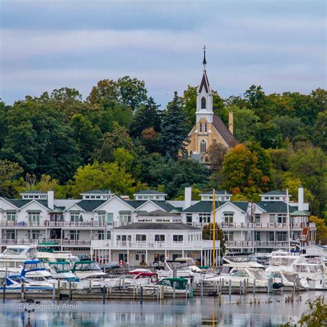 many boats are docked in the water near some buildings and trees with a steeple