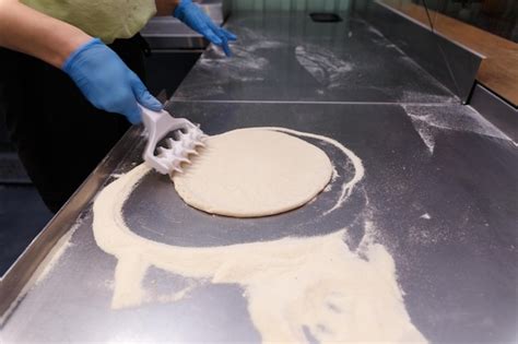 Premium Photo | The cook processes the pizza dough with a special roller with spikes to make the ...