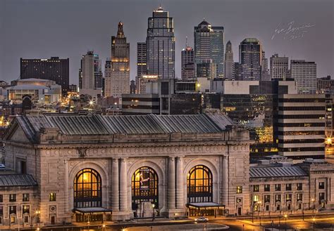 the city skyline is lit up at night, with buildings in the foreground and skyscrapers in the ...