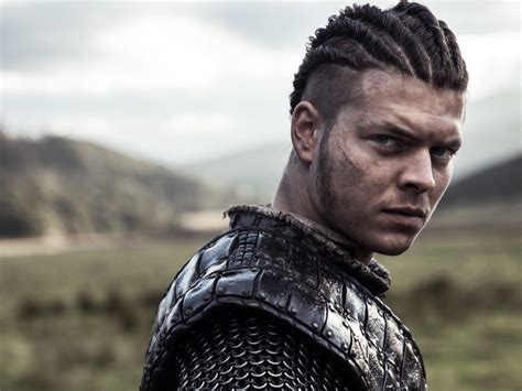 a man in armor with blue eyes stares into the distance while standing on a hill