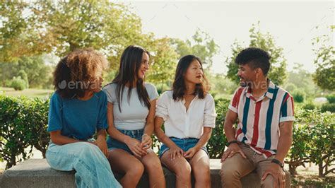 Happy multiethnic young women talking while sitting on park bench on summer day outdoors Stock ...