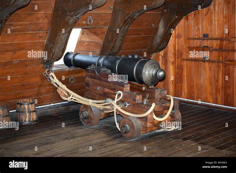 Old iron ships canon positioned on a mobile base with wheels at a porthole on a wooden deck of a ...