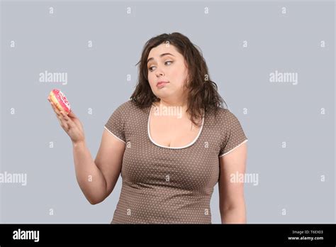 Young stout woman with donut on grey background. Diet food concept Stock Photo - Alamy