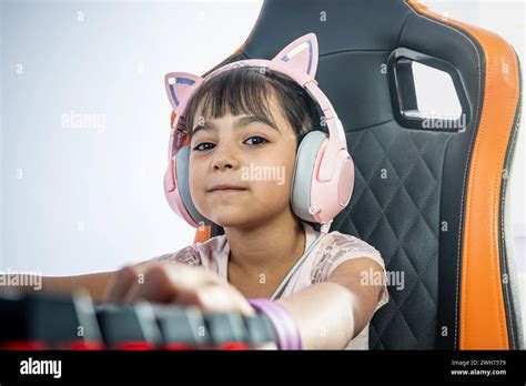 Portrait of a little girl with PC gamer accessories. She looks at the camera. She wears ...