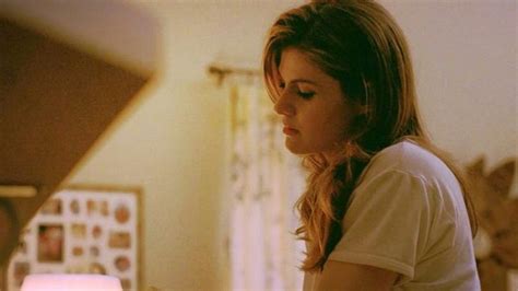 a woman sitting on a bed looking down at her cell phone in the room next to her