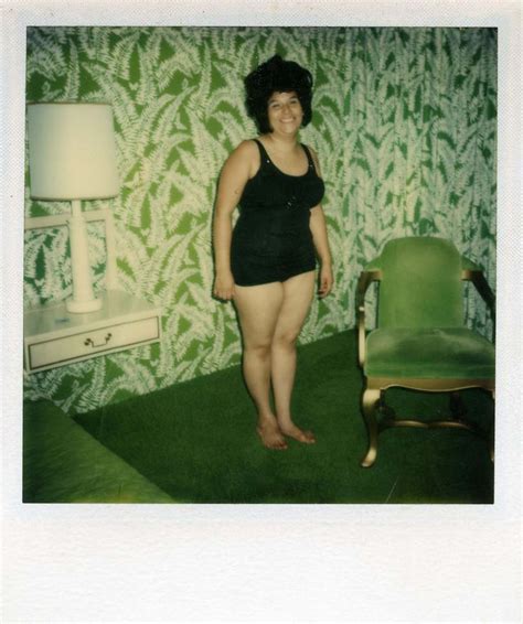 a woman in a black bathing suit standing next to a green chair and wallpaper