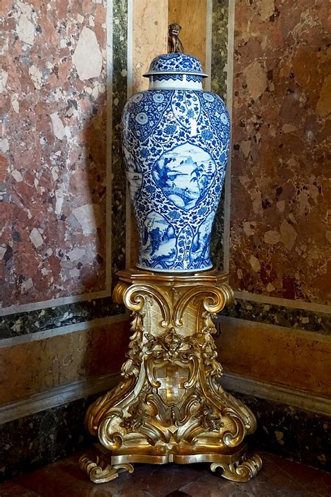 a blue and white vase sitting on top of a golden stand in front of a wall