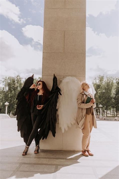 two women dressed in costumes standing next to a tall statue with wings ...